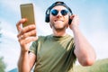 Cool man in baseball cap, wireless headphones and blue sunglasses browsing in his mp3 player playlists smartphone device and Royalty Free Stock Photo