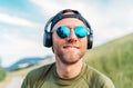 Cool man in a baseball cap, wireless headphones and blue sunglasses smiling and enjoying favorite music playing Royalty Free Stock Photo