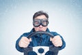 Cool man in a blue jacket and stylish goggles, drives a car in snow with his hands on the steering wheel. Front view