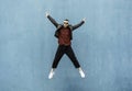 Cool man in casual indie clothes jumping outdoor with open arms against a blue wall background - Trendy guy having fun dancing and Royalty Free Stock Photo