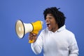 Cool news. Agitated African American teen guy screaming into megaphone over blue studio background Royalty Free Stock Photo