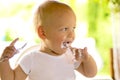 Cool one year kid with a spoon eating a yogurt or sour cream. Outdoor shot Royalty Free Stock Photo