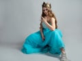 Cool princess in a lush blue dress and crown makes a rocker hand gesture, Royalty Free Stock Photo