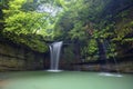 A cool refreshing waterfall pouring into an emerald pond hidden in a mysterious forest of lush greenery Royalty Free Stock Photo