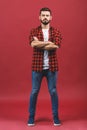 Cool relaxed casual man with crossed arms and titled head looking at camera. Full body length portrait isolated over red Royalty Free Stock Photo