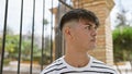 Cool, relaxed young hispanic man looking serious, standing outside on a sunny street