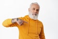 Cool senior man with tattoos pointing at himself. Bearded cool grandfather in orange hoodie self-promoting, bragging