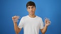 Cool, serious young hispanic man choosing optician\'s glasses, standing in casual wear isolated on blue background, handsome face