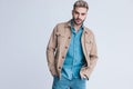 Cool sexy man in denim shirt and beige jacket holding hands in pockets