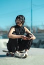 Cool skater girl wearing eyeglasses using her phone while sitting on skateboard in the floor