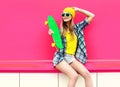 cool smiling woman with skateboard wearing colorful yellow hat on pink Royalty Free Stock Photo