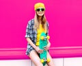 cool smiling woman with skateboard wearing colorful yellow hat on pink Royalty Free Stock Photo