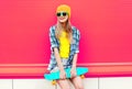 cool smiling woman with skateboard wearing colorful yellow hat on pink Royalty Free Stock Photo