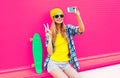 cool smiling woman taking selfie picture by smartphone with skateboard wearing colorful yellow hat on pink Royalty Free Stock Photo