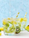 Cool soda water poring into yellow watermelon and kiwi lemonade with ingredients on bright blue background. Motion. Vegeterian foo