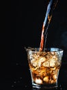 Cool, soft carbonated cola drink is poured into a glass of ice. Soda water refreshing drink isolated on dark background Royalty Free Stock Photo