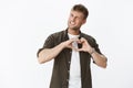 Cool and stylish confident handsome man winking, smiling cheeky and flirty at camera showing heart gesture confessing in