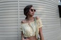 Cool stylish young hipster girl with sunglasses in a fashionable summer blouse with a bag walks on the street Royalty Free Stock Photo