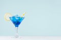 Cool summer blue beverage margarita for party with ice cubes, lemon slice, yellow straw on white wood board and mint color wall. Royalty Free Stock Photo