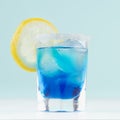 Cool summer blue beverage margarita for party with ice cubes, salt rim, lemon slice on white wood board and mint color wall. Royalty Free Stock Photo