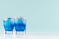 Cool summer blue beverage margarita for party with ice cubes, salt rim in two wet shot glasses on white wood board and mint color. Royalty Free Stock Photo