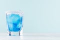 Cool summer blue beverage margarita for party with ice cubes, salt rim on white wood board and mint color wall. Royalty Free Stock Photo