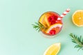 Cool summer drink with lemon, raspberry and rosemary in glass with striped eco straw on green background