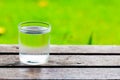 Cool water glass on wooden table with grass field background. Royalty Free Stock Photo