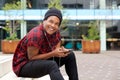 Cool young african american man sitting in city with mobile phone and headphones Royalty Free Stock Photo