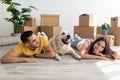 Cool young diverse couple lying on floor among carton boxes with their cute dog, relocating to new home with pet Royalty Free Stock Photo