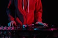 Cool young DJ in red hoodie scratching vinyl records on turntables in night club. Hands of a hip hop disc jockey playing music on Royalty Free Stock Photo