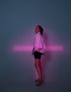 Cool young girl standing with cross shaped pink neon light in studio