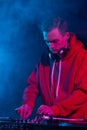Cool young hip hop DJ in red hoodie mixing vinyl records on a party in night club. Professional disc jockey plays set in smoke on Royalty Free Stock Photo