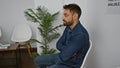 Cool young hispanic man, arms crossed in a relaxed gesture, sitting in a waiting room chair with a serious expression, looking Royalty Free Stock Photo