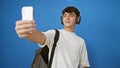 Cool young hispanic teenager guy, a smiling student engrossed in a lively video call conversation, standing isolated against a Royalty Free Stock Photo