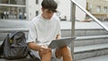 Cool young hispanic teenager, a smart university student engrossed in online study on laptop while sitting casual on stairs at Royalty Free Stock Photo