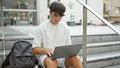 Cool young hispanic teenager, a smart university student engrossed in online study on laptop while sitting casual on stairs at Royalty Free Stock Photo