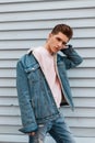 Cool young man with serious face with trendy hairstyle in fashionable blue denim casual wear posing near vintage white wall on Royalty Free Stock Photo