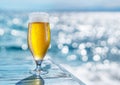 Cooled glass of beer with condensation drops on the blue wooden table. Blurred sea is at the background Royalty Free Stock Photo