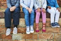 The coolest kids at school. a group of unrecognizable elementary school kids sitting on a brick wall outside.