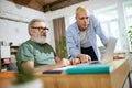 Cooperation of adults and youngsters. Young man helping senior businessman with technological issues on laptop