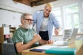 Cooperation of adults and youngsters. Young man helping senior businessman with technological issues on laptop