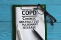 COPD - acronym in a notepad on a blue background with a pen, glasses and a thermometer