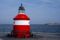 A small red-white-striped lighthouse on the shore. A small island in the background Royalty Free Stock Photo