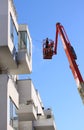 Man cleaning facade of a modern minimalistic apartment building on a telescopic boom lift using pressure jet wash blue sky backgro
