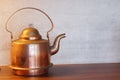 Copper or brass kettle stands on the table opposite the gray wall