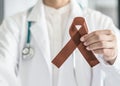 Copper Brown Awareness Ribbon on doctorÃ¢â¬â¢s hand, symbolic color for Anti-Tobacco, Colon Colorectal Cancers, Herpes Simplex Virus