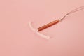 Copper intrauterine contraceptive device on light pink background