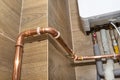 Copper pipes for natural gas installations, attached to a wall in a boiler room lined with ceramic tiles.