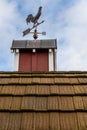 Copper rooster weathervane on top of red rooftop cupola with a blue sky and white clouds in the background